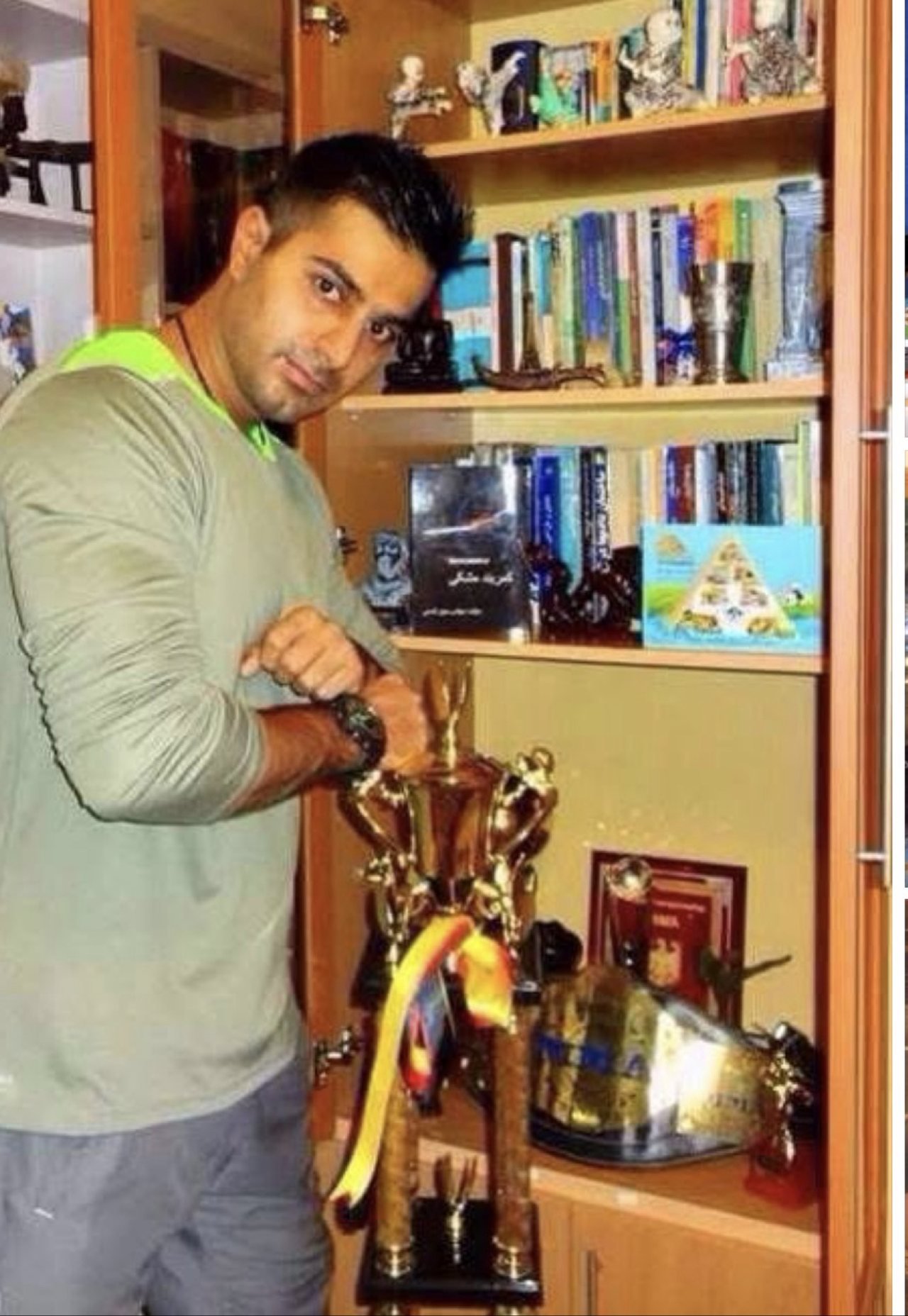 Mah Ghasemi beside a bookshelf of books and a championship trophy cup