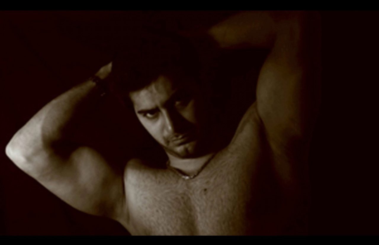 Mah Ghasemi in a sepia portrait, arms raised behind his head in a stretch